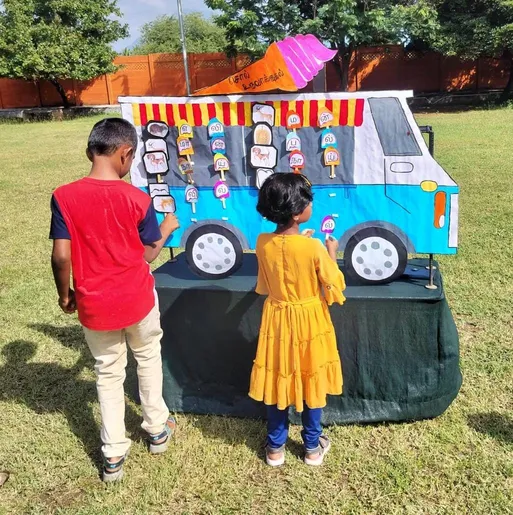 Children at Vidhya Peetham i-School spelling out Tamil words with letter cards on an ice-cream vehicle chart, highlighting innovative learning methods.