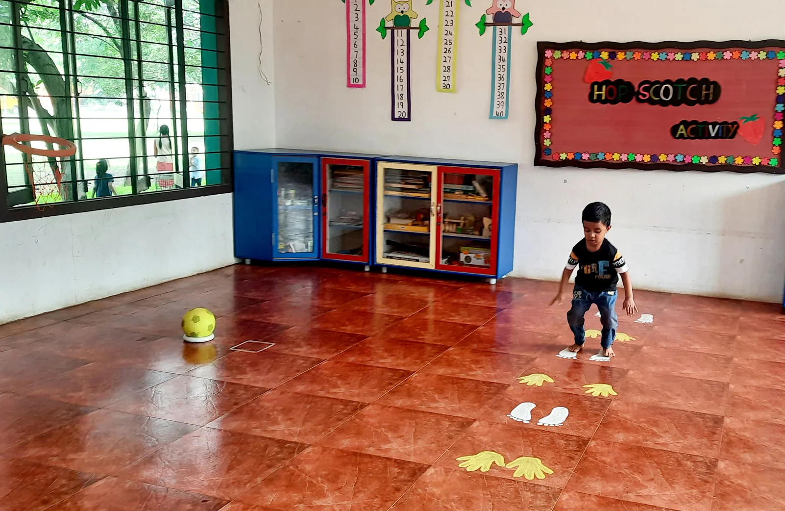 Determined LKG student carefully navigating hand and footprints in hopscotch, demonstrating cognitive and motor skills development at Vidhya Peetham i-School.