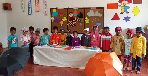 Vidhya Peetham i-School's LKG class in Salem poses with umbrellas and seasonal attire, demonstrating their knowledge of the different weather conditions.