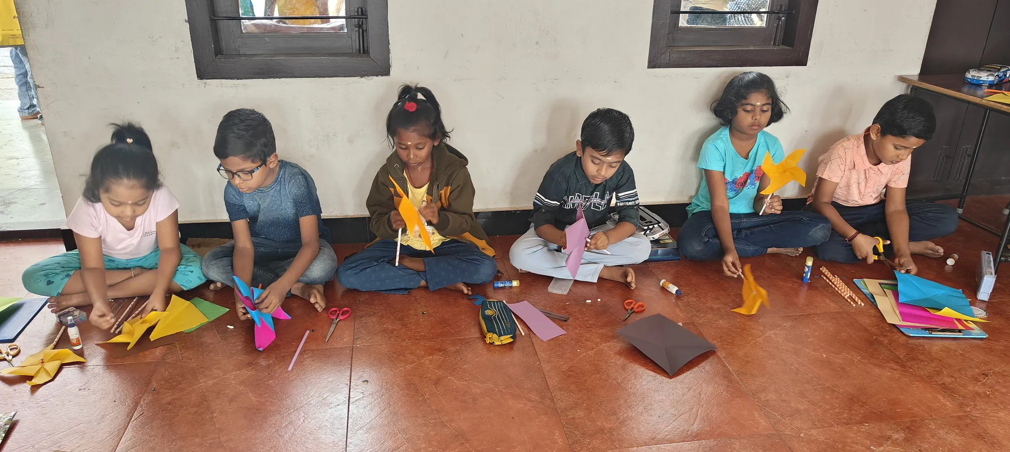 Vidhya Peetham i-School children in the midst of a pinwheel-making session, surrounded by vibrant art materials.