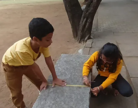 Budding scientists from the best school in Salem meticulously measuring a stone bench during their measurement activities.