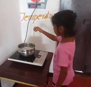 A young student measuring water temperature on a stove with a thermometer at a leading CBSE school in Salem.