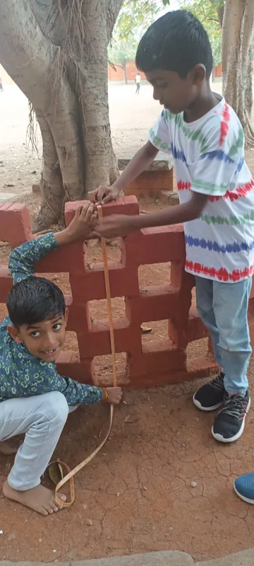 Inquisitive students at one of the top schools in Salem measuring bricks with a tape measure outdoors.