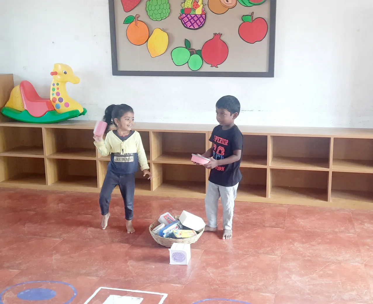 Young learners engaging with shapes, with a colorful fruit chart in the background, at one of the best CBSE schools in Salem. ??