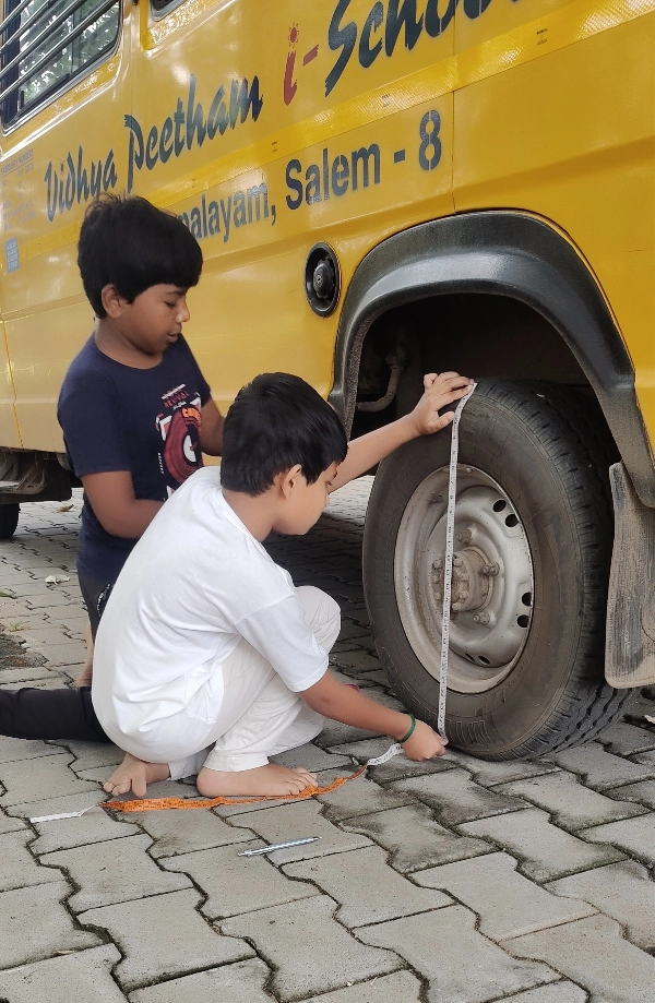Children using a measuring tape to find the circumference of a school bus tire at one of the top schools in Salem.