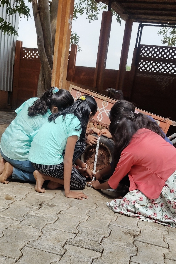 Group of girls measuring the circumference of a large wheel during a math activity at the best school in Salem.