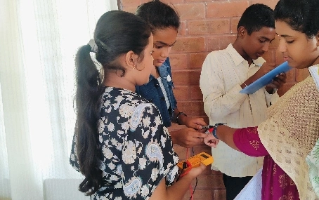 Students checking conductivity with a multimeter during a practical session in the basics of electronics workshop.