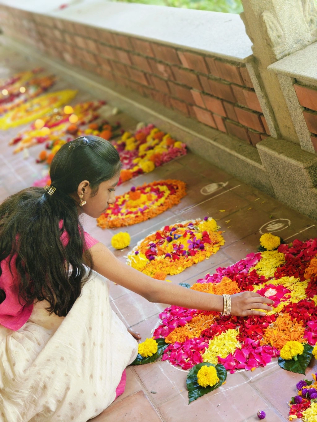 A girl laying a flower rangoli, with rows of bright flower patterns behind her