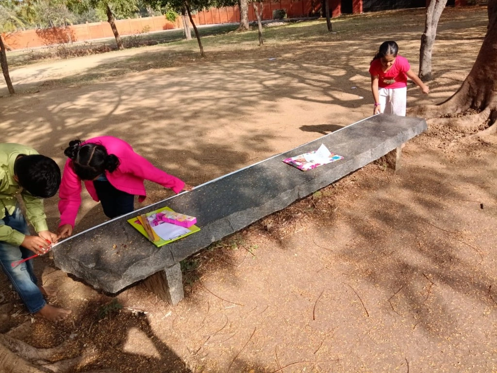 Students measuring length of stone bench outdoors for the area and perimeter of squares and rectangles activity