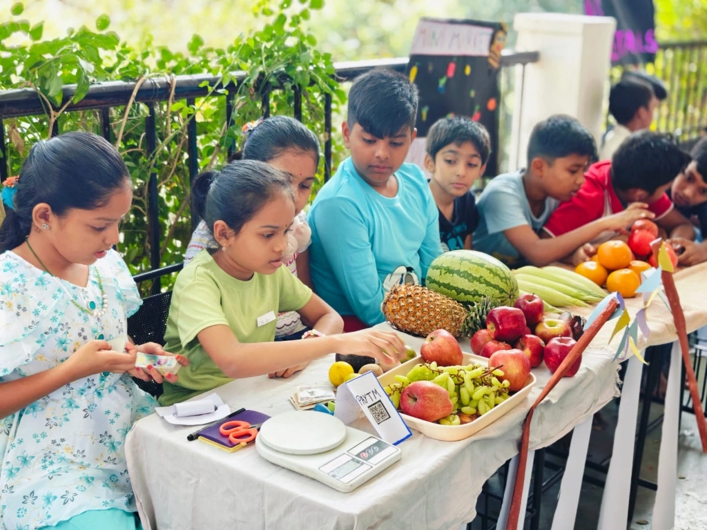 Students engaged in fruit market calculations with fresh produce display