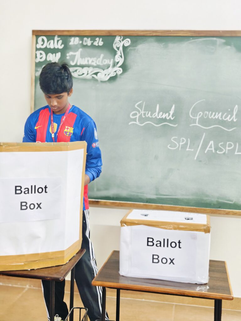 SPL and ASPL elections: a student stands at a cardboard ballot box before a chalkboard reading Student Council SPL/ASPL.