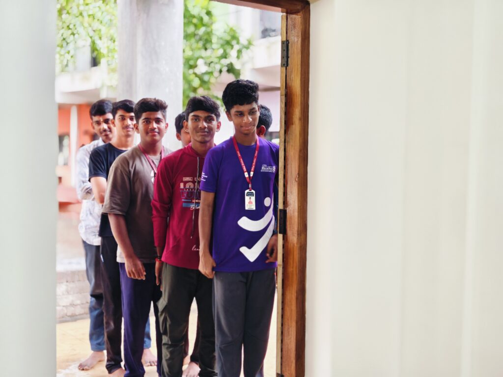 A line of boys waits at a classroom doorway for their turn to vote.
