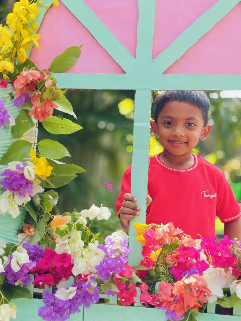 A smiling child in a red T-shirt holds the mint frame of the flower-decorated window booth.