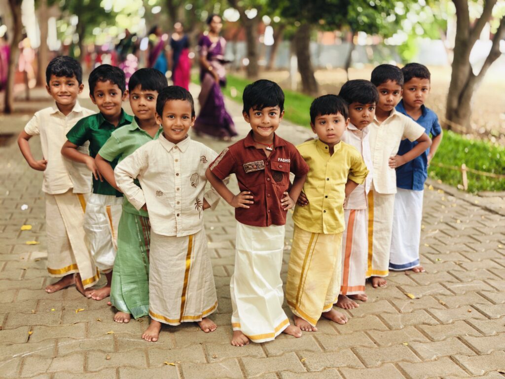 Young boys in coloured shirts and veshtis pose with hands on hips on a paved path