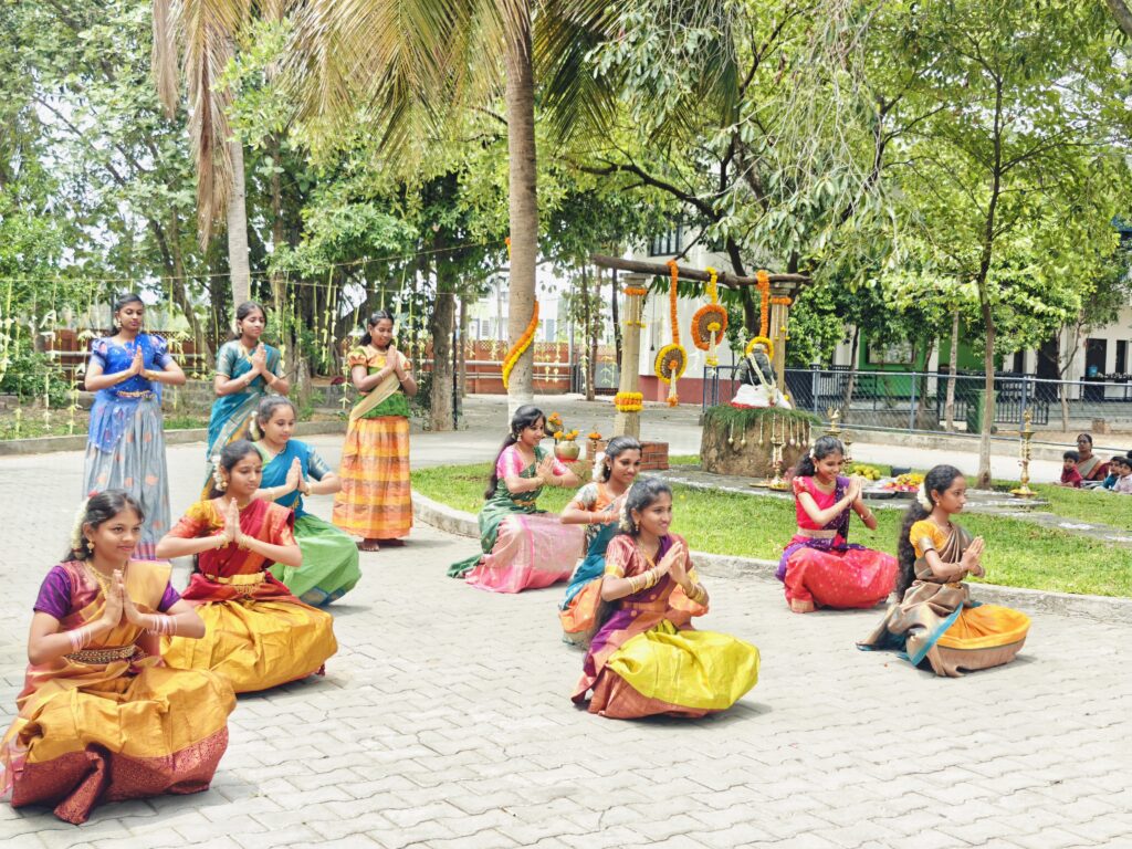 Girls in silk pavadai and half-sarees perform a dance with palms joined near the decorated shrine