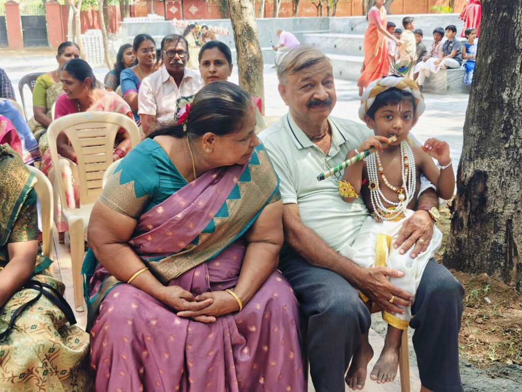 An elderly couple sit with a young child in costume holding a flute on his lap.