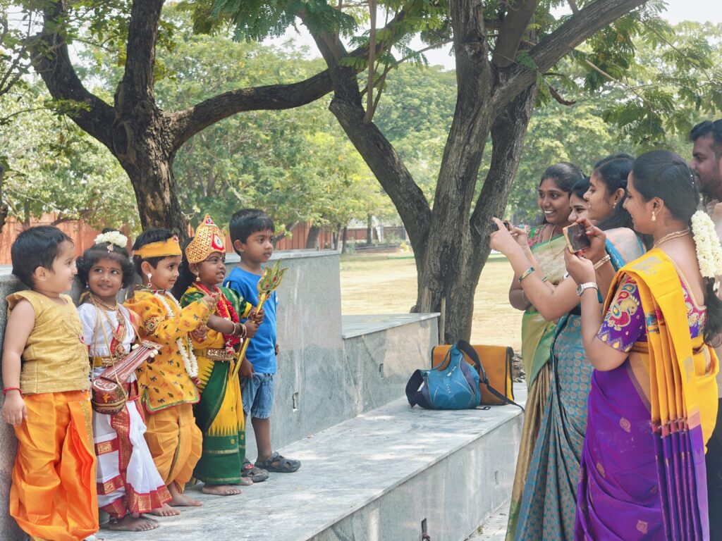 Young children in traditional costumes pose on a stone ledge as women photograph them with phones.