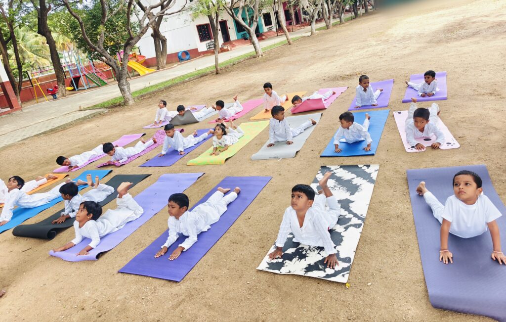 Young children lie face down on mats outdoors, lifting their chests with hands on the ground.