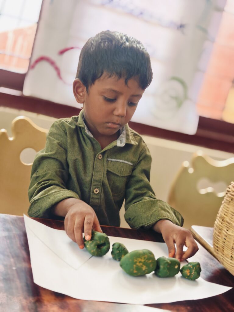 Child in a green shirt arranges green pieces along a drawn line on white paper.