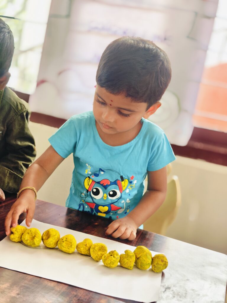 Child in a blue T-shirt arranges yellow pieces along a long line on white paper.