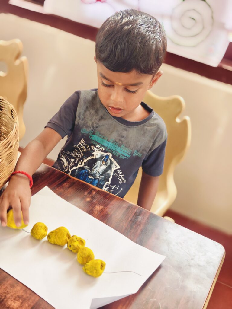 Child in a grey T-shirt sets yellow pieces along a straight line on paper beside a woven basket.