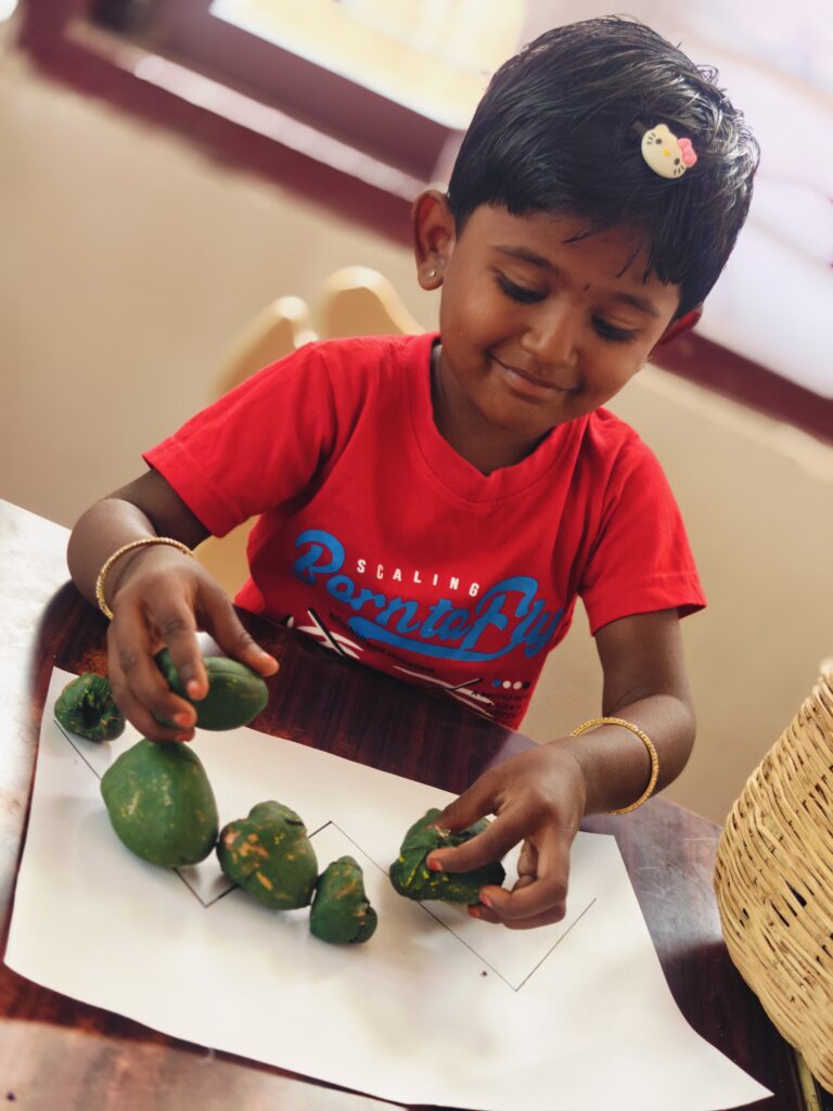 Child in a red T-shirt places green pieces along a zigzag line drawn on paper.
