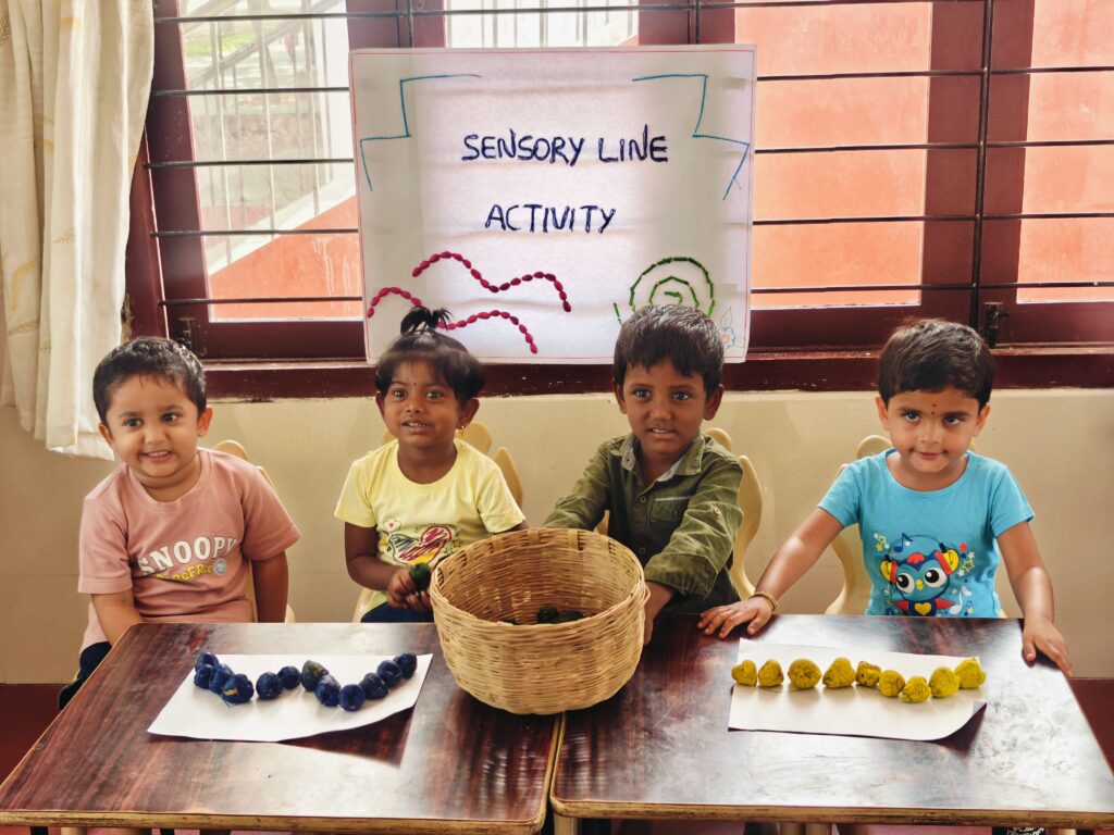 Four children smile behind a table with lines of blue and yellow pieces and a woven basket.