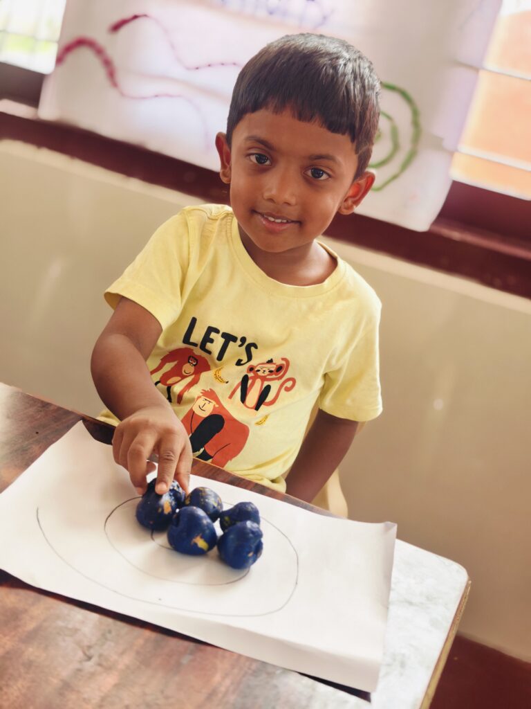 Smiling child in a yellow T-shirt places blue pieces on a circle drawn on white paper.
