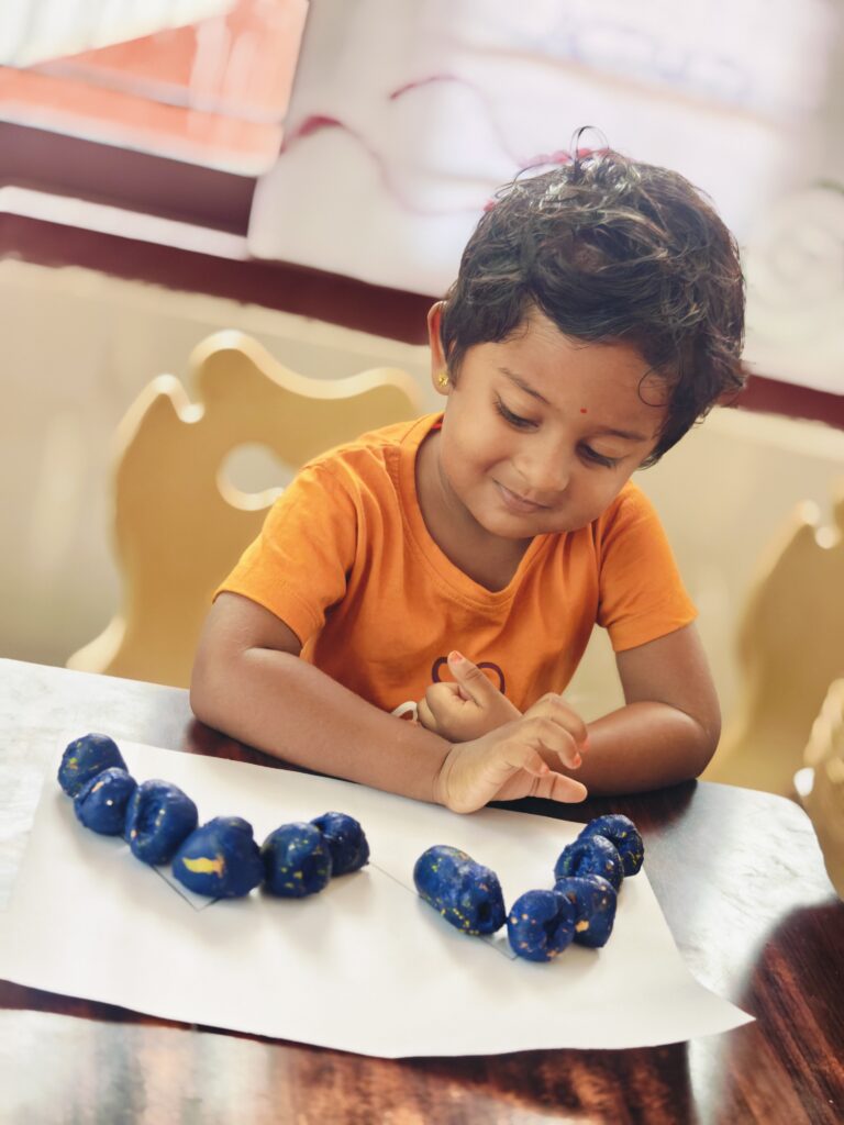 Smiling child in an orange T-shirt looks at a row of blue pieces arranged along a drawn line.