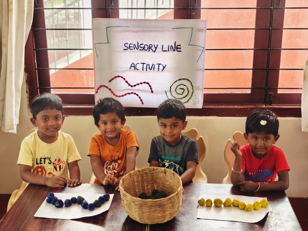 Four children sit behind a woven basket and two finished lines of blue and yellow pieces.