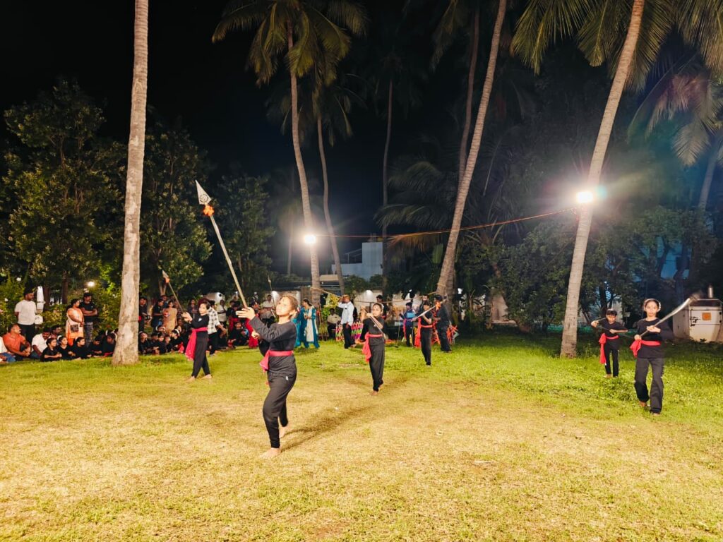 Students in black with red sashes move across the lawn holding spears and short swords