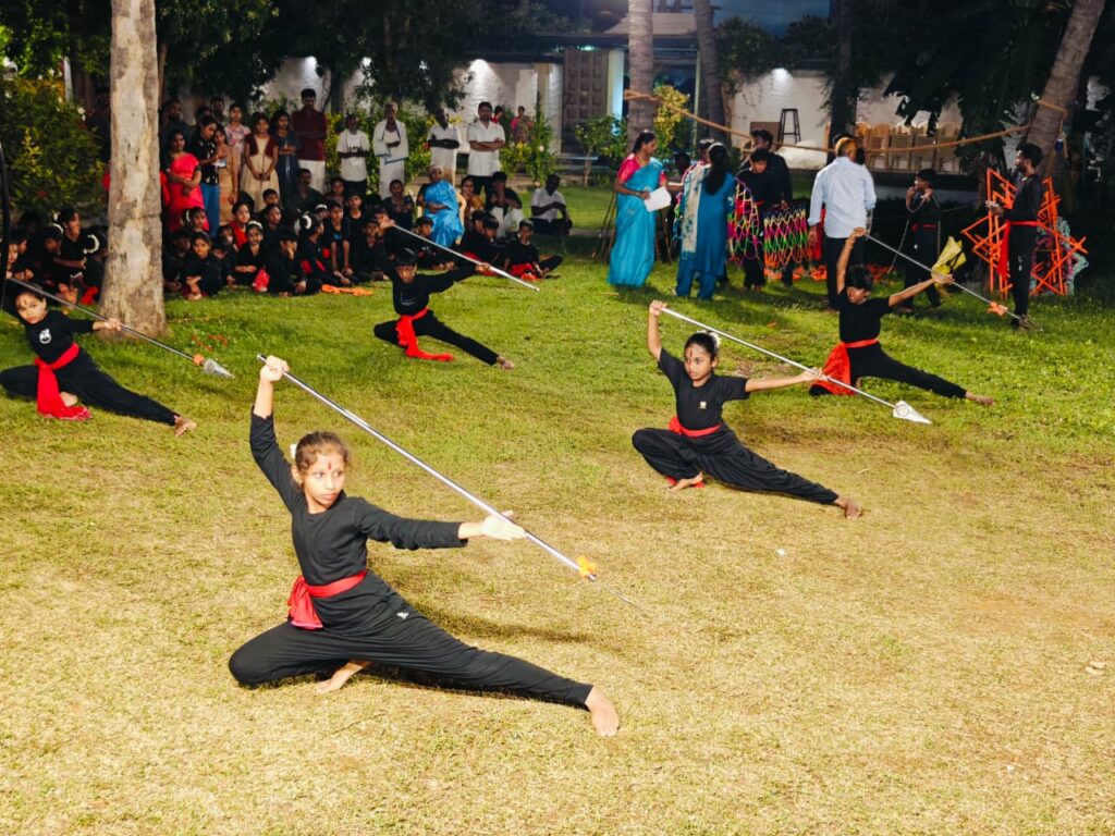 Students in black with red sashes hold long spears in deep lunging stances on the grass