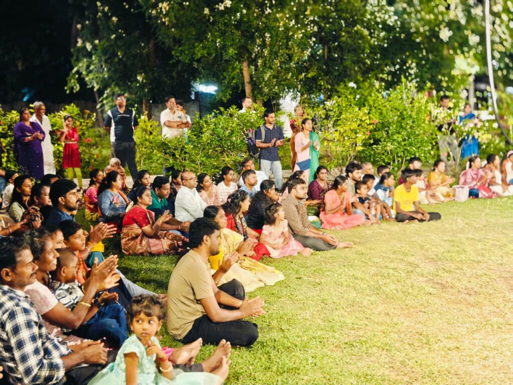 Families sit on the grass watching the performance, some clapping